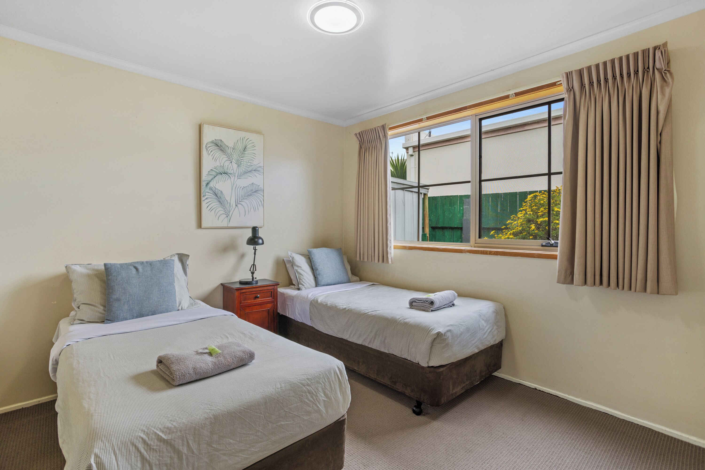 A bedroom with two beds, a nightstand, a lamp, and a window with curtains.