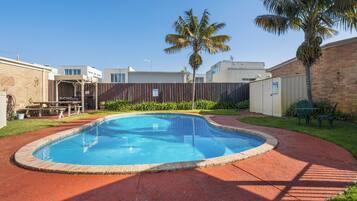 Una piscina con borde de ladrillo, rodeada de un patio rojo.