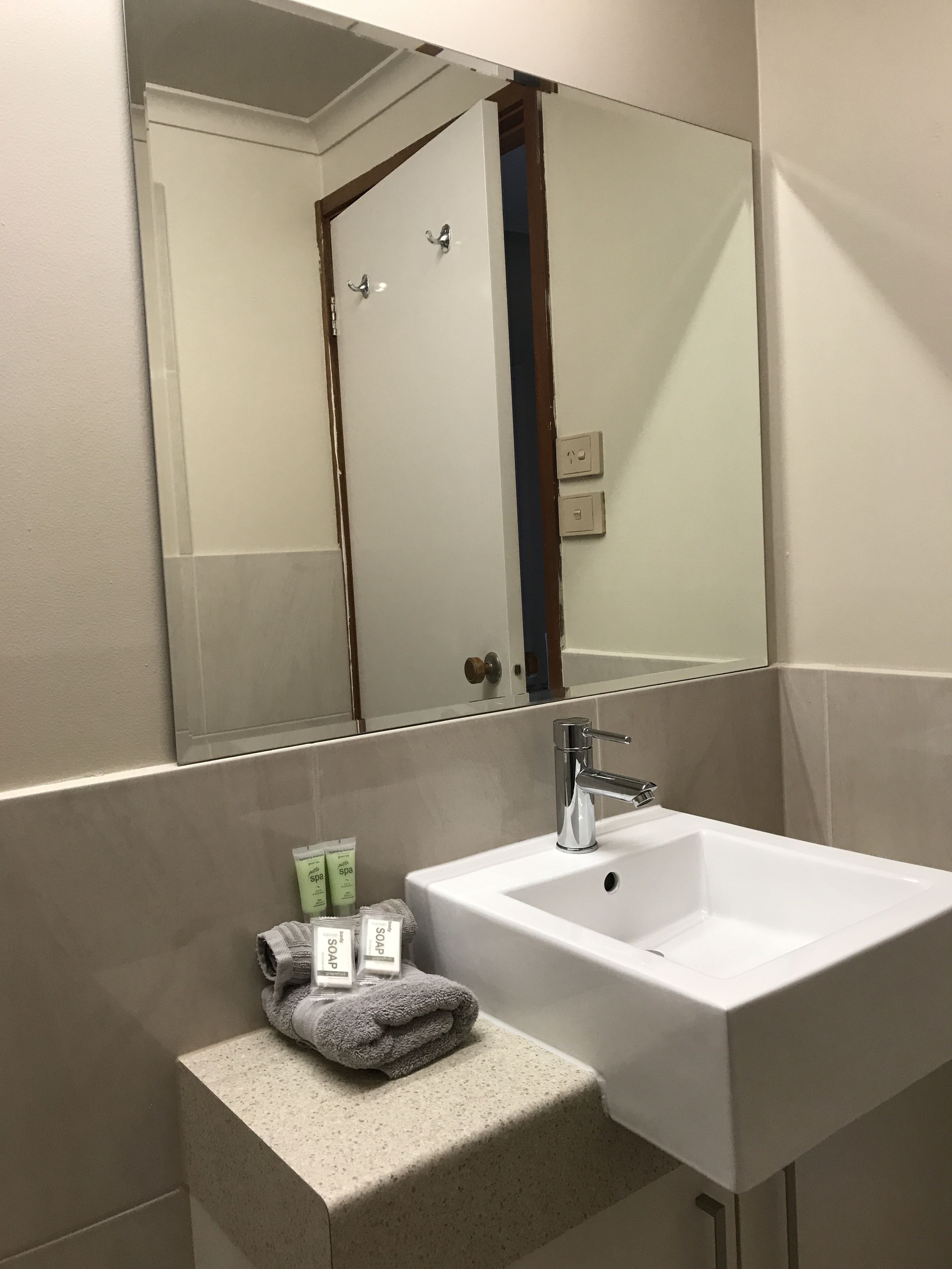 A bathroom with a white sink, a mirror, and a towel dispenser.