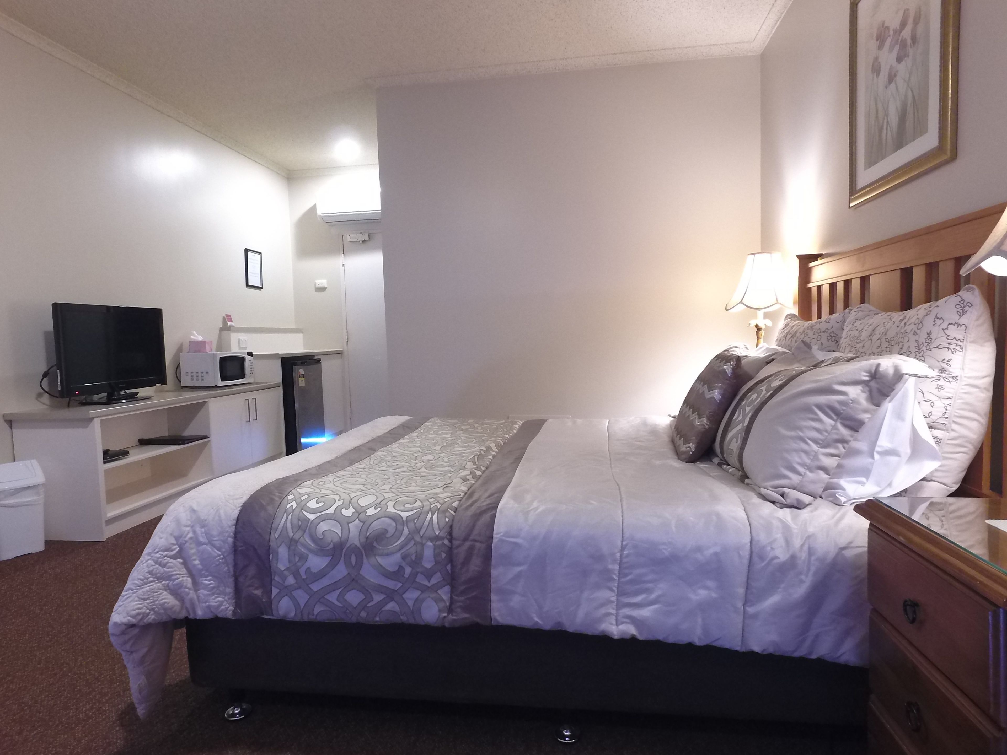 Una habitación de hotel ordenada con cama, mesita de noche, lámpara y televisor sobre un escritorio.