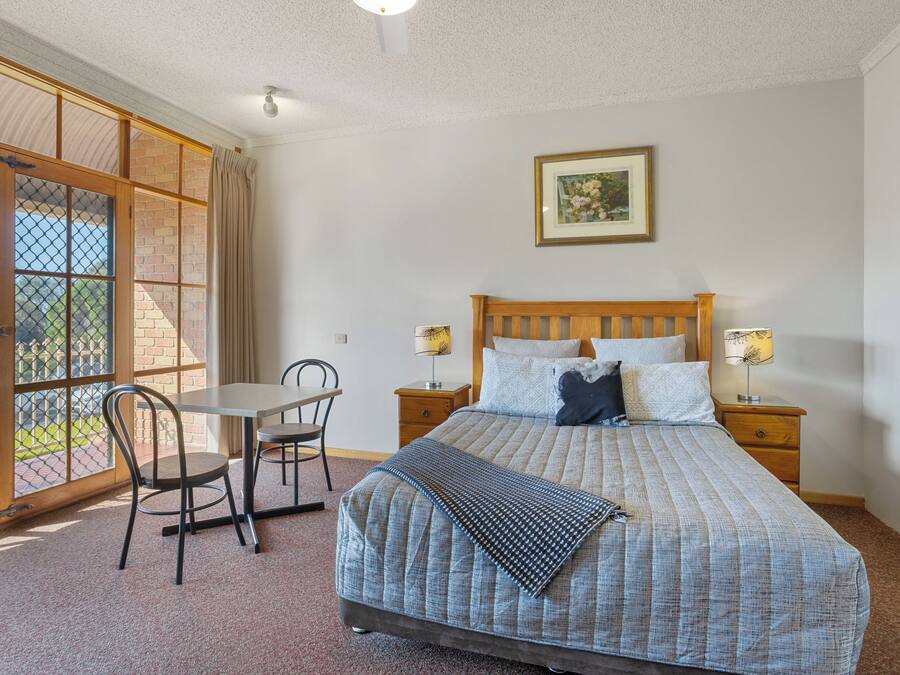Une chambre à coucher comprenant un lit, des tables de chevet, une chaise, une table et une fenêtre donnant sur un beau paysage.