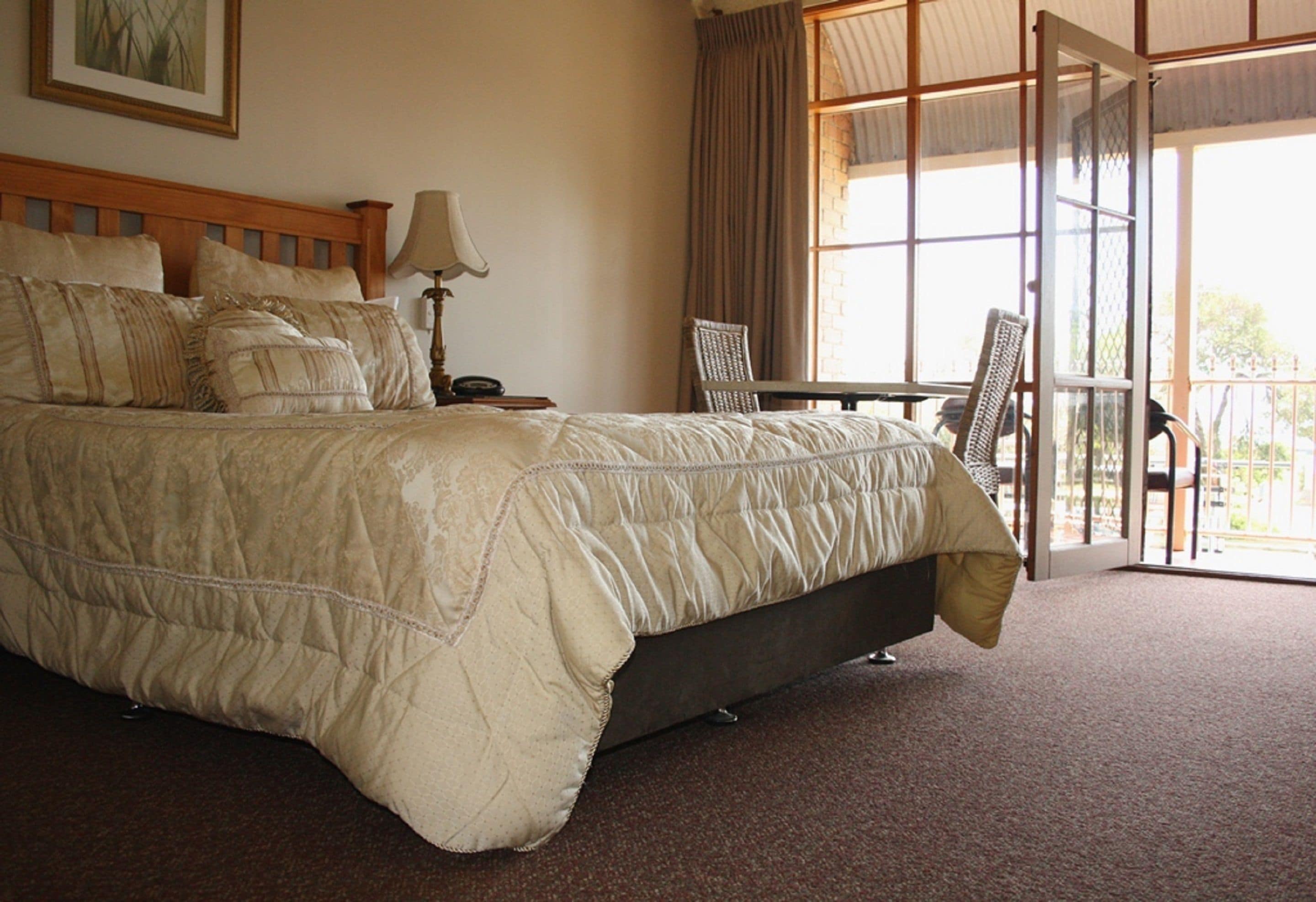 A bedroom with a large bed, a nightstand, a lamp, and a view of the outdoors through a glass door.