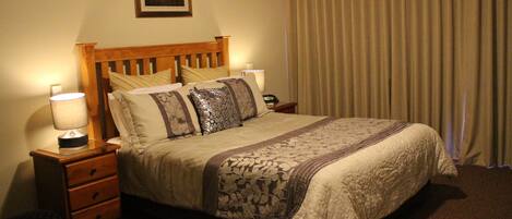 A neatly made bed with a patterned bedspread and pillows, a bedside table with a lamp, and a framed picture on the wall.