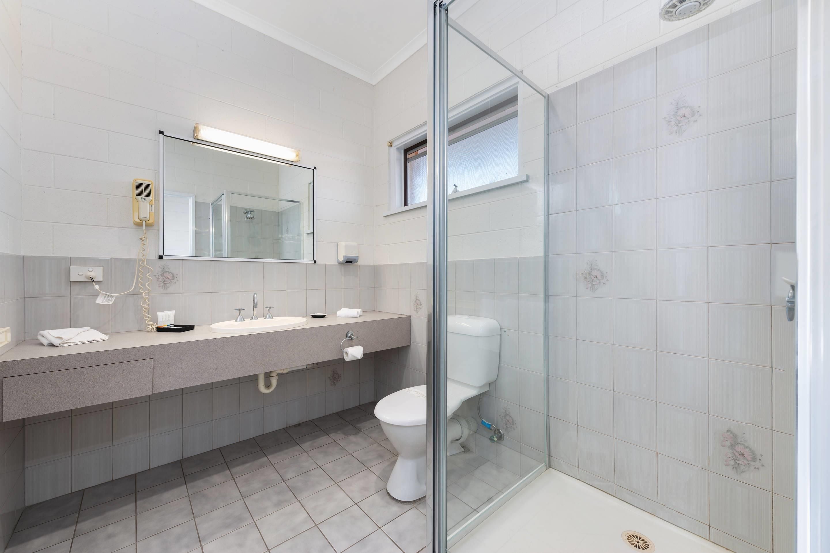 Un baño moderno con cabina de ducha de vidrio, un espejo grande y un tocador con lavabo y toallero.