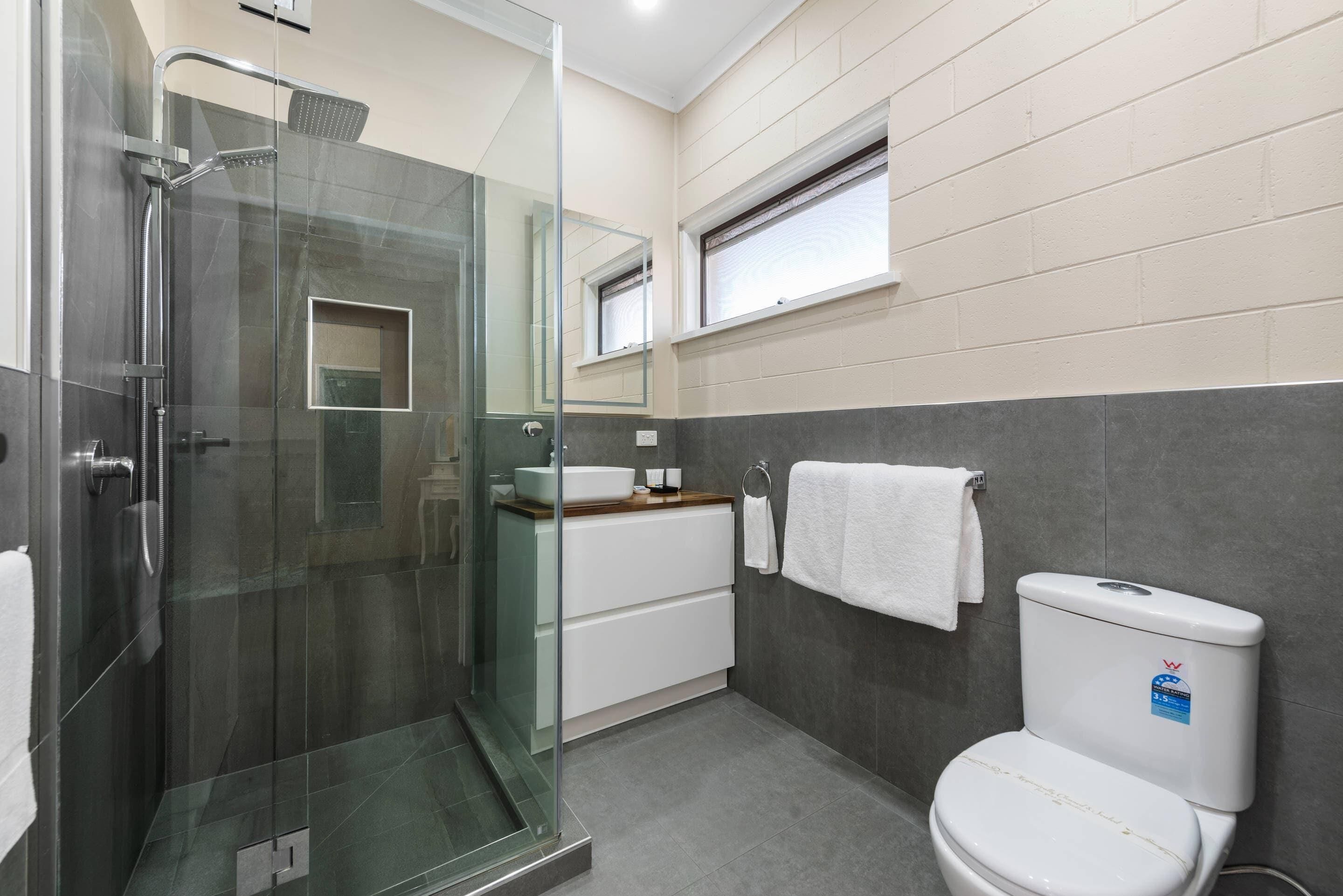 Un baño moderno con ducha envuelta en vidrio, inodoro blanco y lavamanos con encimera de madera.
