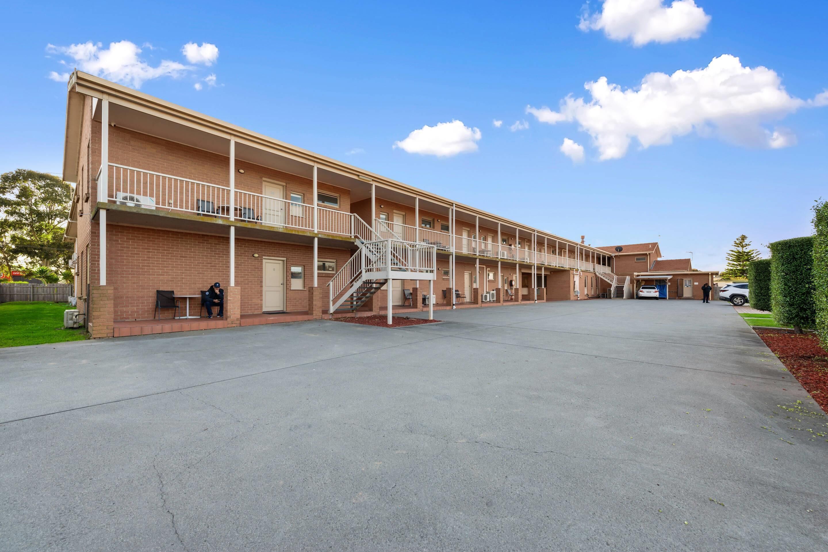 A multi-story motel with a central staircase, outdoor seating, and a parking area.