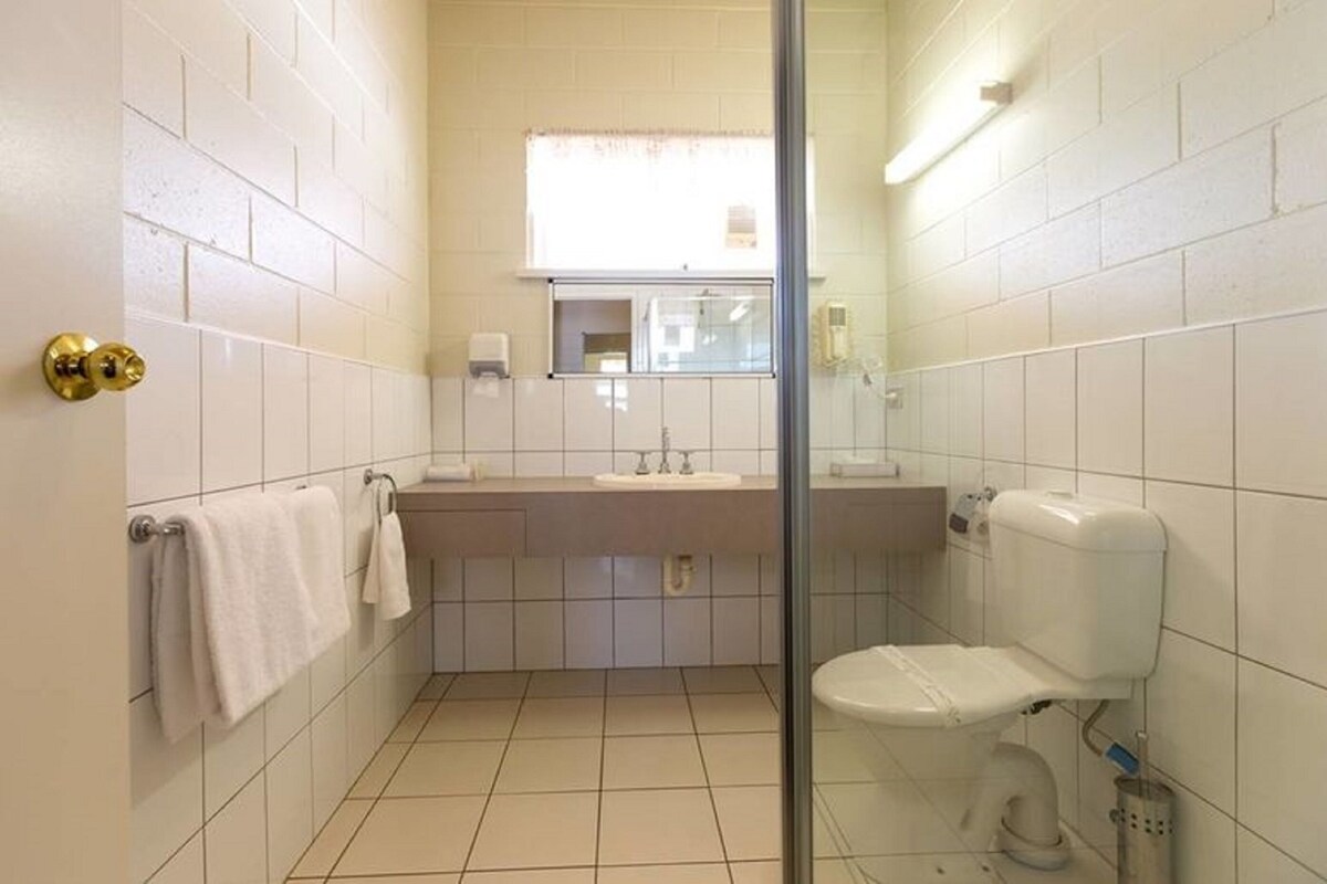 A bathroom with white tiled walls, a glass shower enclosure, a toilet, and a sink with a mirror above it.