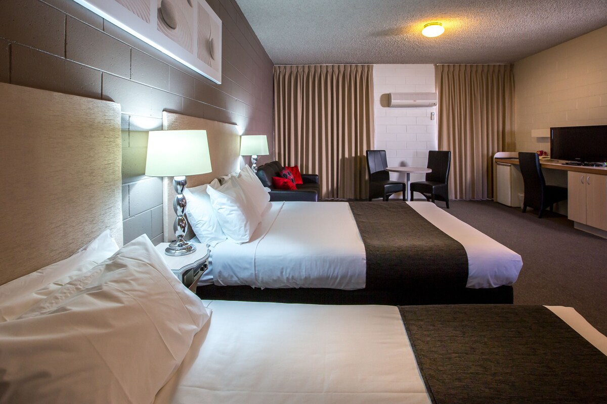 A hotel room with two beds, a desk, a chair, and a television.