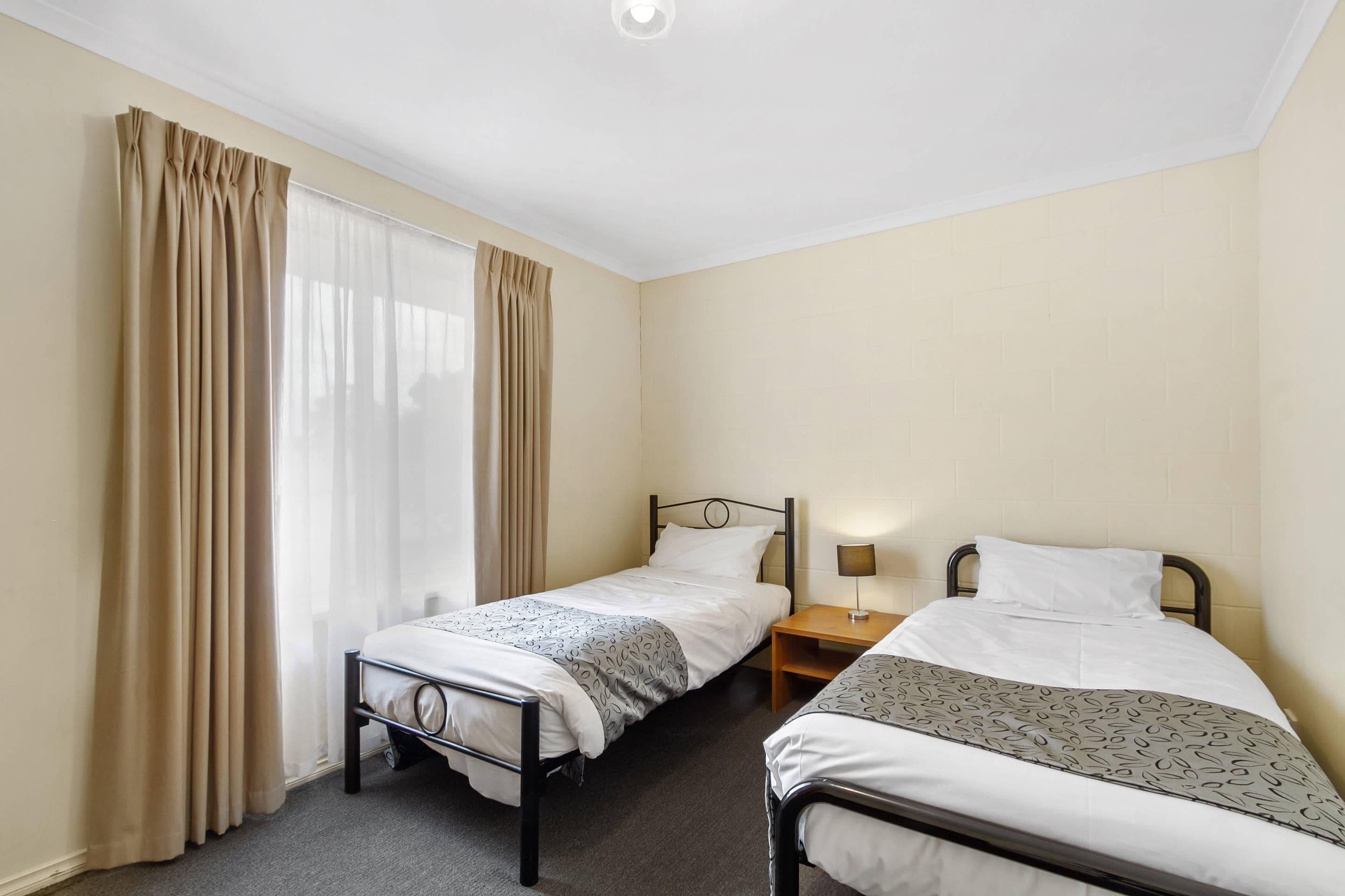 A twin room with two single beds, a nightstand with a lamp, and a window with curtains.