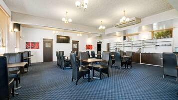 A hotel dining area with multiple tables and chairs, a reception desk, and a wall-mounted television.