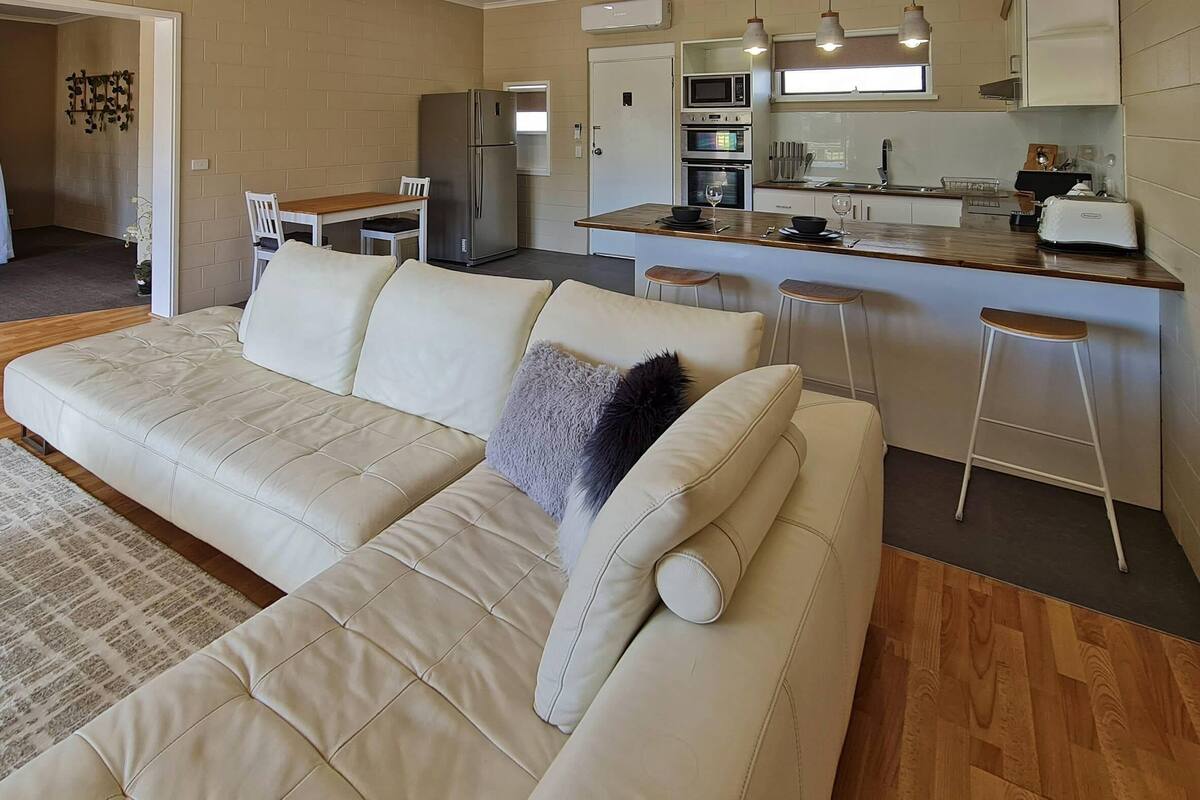 A modern living room with a sofa, a dining area, and a kitchenette.