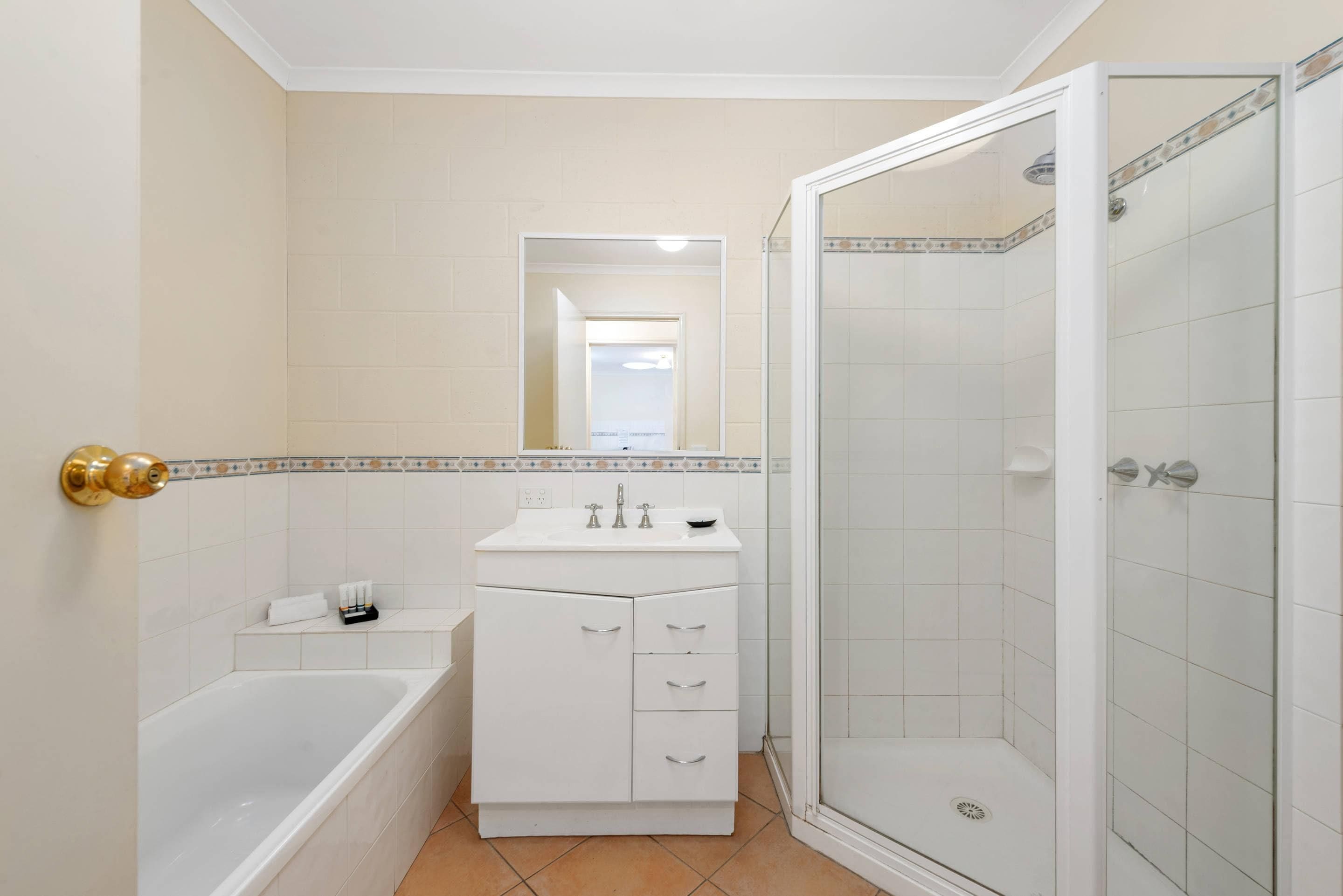 A bathroom with a bathtub, a sink with a mirror, and a shower enclosure.