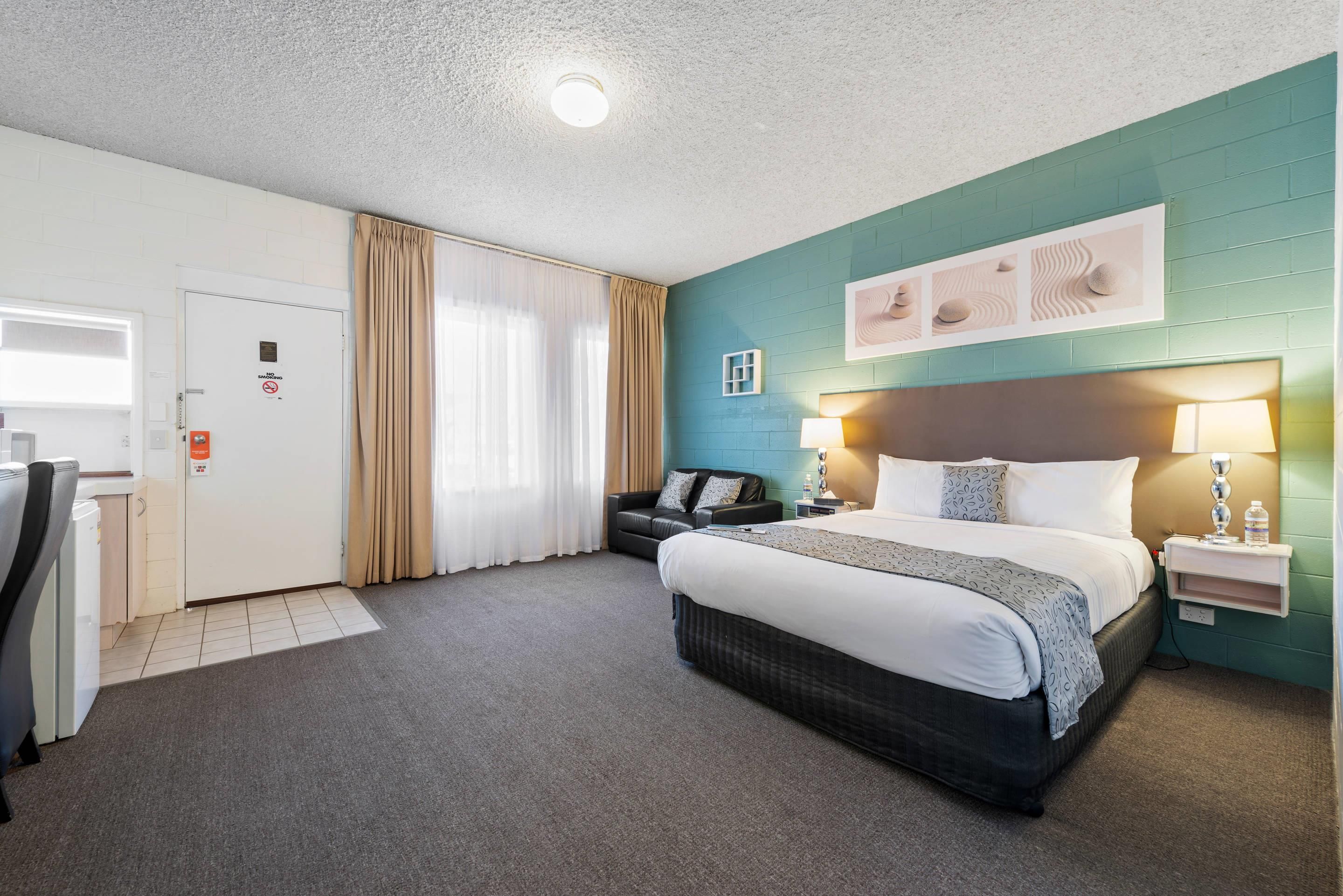 Quarto de hotel com cama, escrivaninha, cadeira, armário e banheiro.