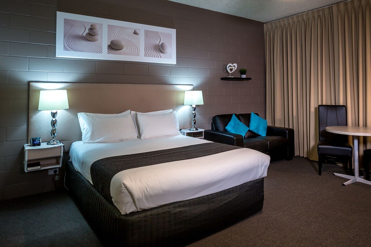 A hotel room with a large bed, two bedside tables with lamps, a sofa, a chair, and a desk.