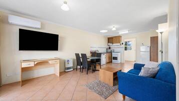 A modern apartment with a living room, dining area, kitchenette, and a TV mounted on the wall.