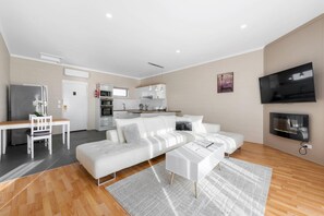 A modern living room with a white sofa, a dining table, and a kitchen in the background. - Comfort Inn & Suites King Avenue (Sale)