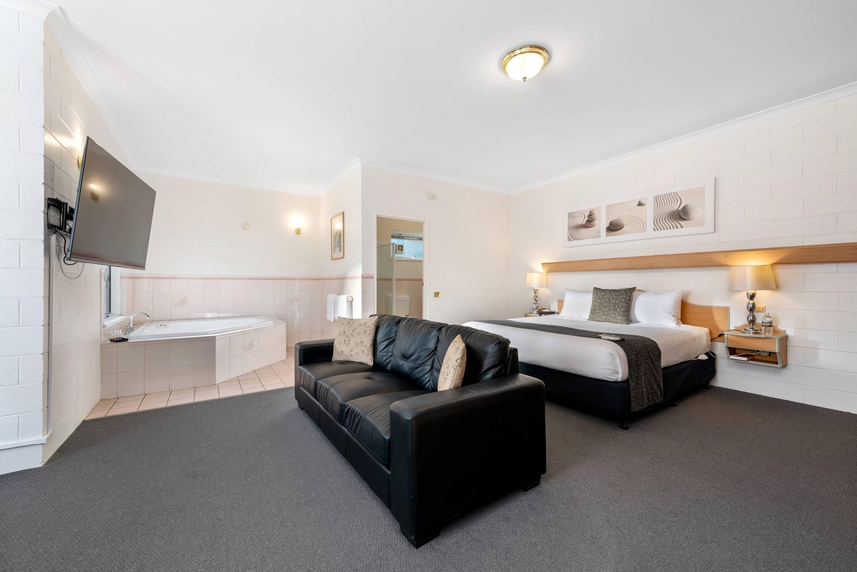 A hotel room with a bed, a sofa, a TV, a bathroom, and a wall-mounted artwork.
