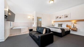 A hotel room with a bed, a sofa, a TV, a bathroom, and a wall-mounted artwork.