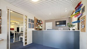 A reception area with a blue carpet, a reception desk, a mounted television, and a bulletin board with multilingual welcome signs. - Comfort Inn & Suites King Avenue (Sale)