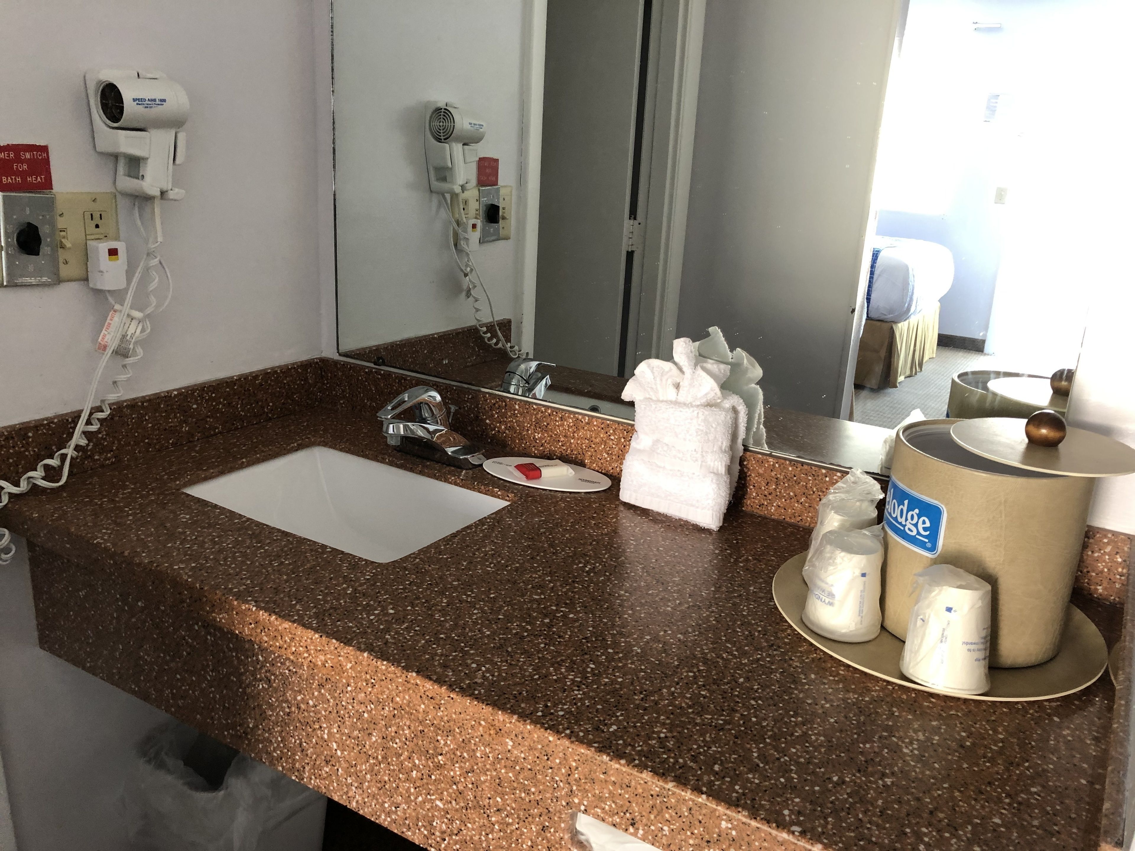 Ein Hotelbadezimmer mit einer Granit-Arbeitsplatte, einem Waschbecken, einem Spiegel, einem Fön, einem Handtuchspender und einem Seifenspender.