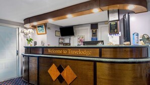 Una recepción con un cartel de "Welcome to Travelodge", certificados enmarcados, un televisor y un cartel de "No se admiten mascotas".