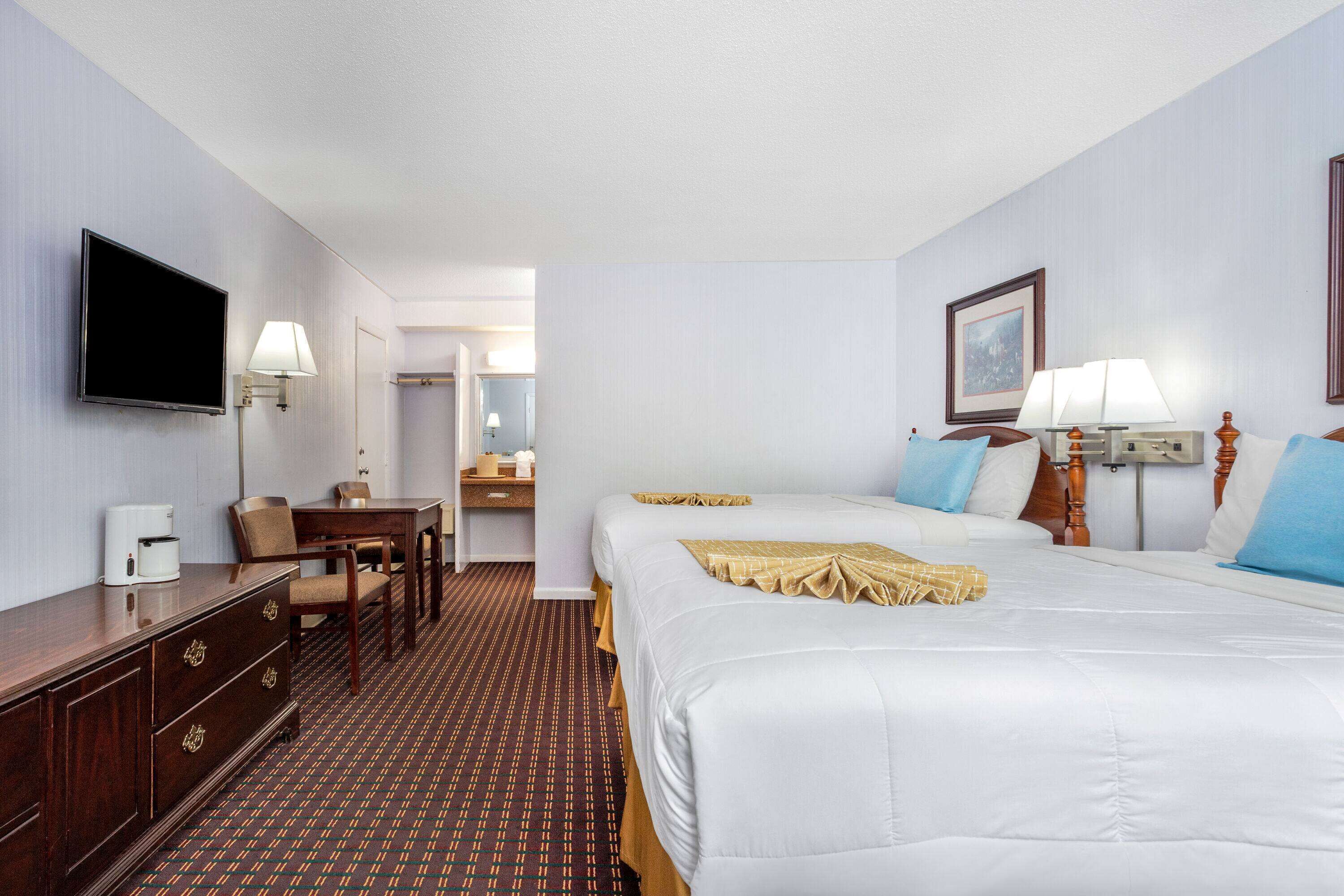 Ein Hotelzimmer mit einem großen Bett, einem Schreibtisch mit Stuhl, einem Fernseher und einem durch eine offene Tür einsehbaren Badezimmer.