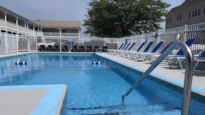 Una piscina con un cartel de 'No Diving', rodeada de barandillas blancas y sillas reclinables azules.