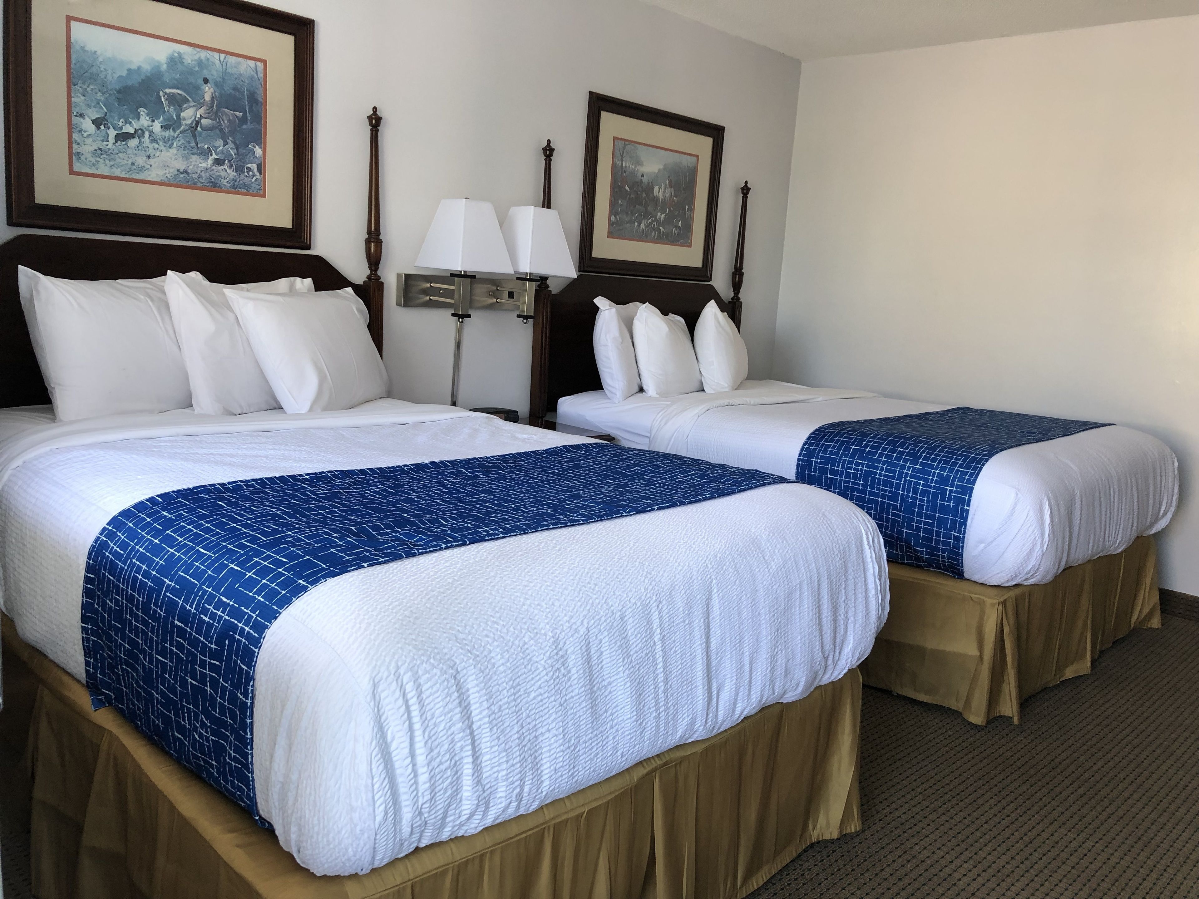 Une chambre d’hôtel avec deux lits, chacun agrémenté de draps blancs et de touches de couleur bleue. Deux lampes murales et des tableaux encadrés sont disposés au-dessus des lits.