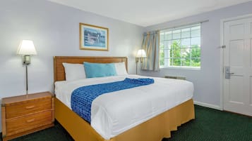 A neatly made bed with a blue and white bedspread, a wooden nightstand with drawers, a framed picture on the wall, and a window with curtains.