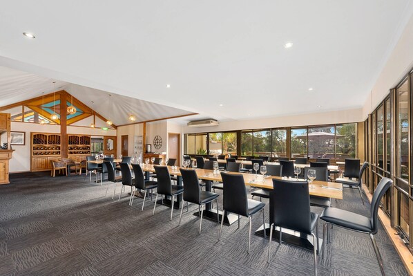 A spacious conference room with multiple tables and chairs, large windows, and a wooden ceiling structure.