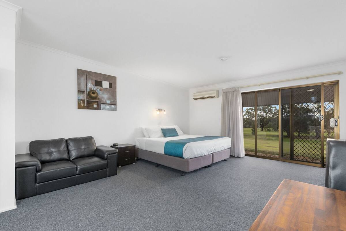 A hotel room with a bed, a sofa, a small table, and a sliding glass door to the outside.