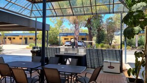 An outdoor patio with tables and chairs, a covered area with a metal roof, and a view of buildings and trees in the background. - Comfort Inn & Suites Riverland (Barmera)