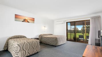 Habitación de hotel con dos camas, un cuadro de un atardecer sobre el agua, una puerta corrediza de vidrio a un balcón y una mesa de madera.