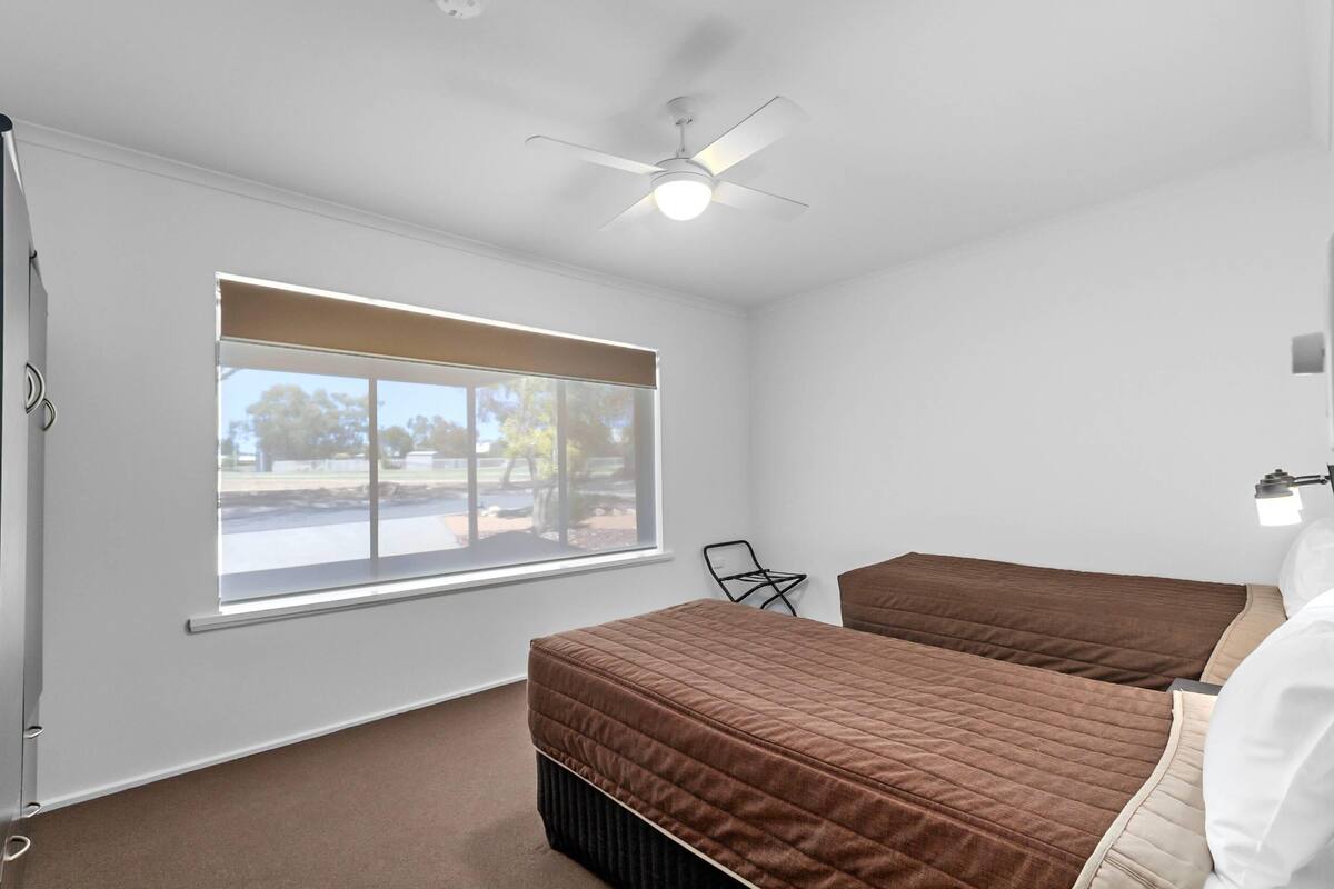 A bedroom with two beds, a ceiling fan, a window with blinds, and a chair.