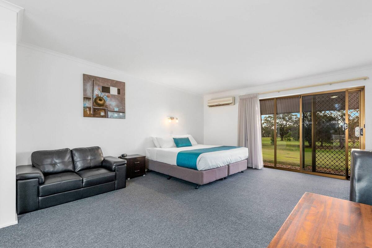 A hotel room with a bed, a sofa, a table, and a painting on the wall.
