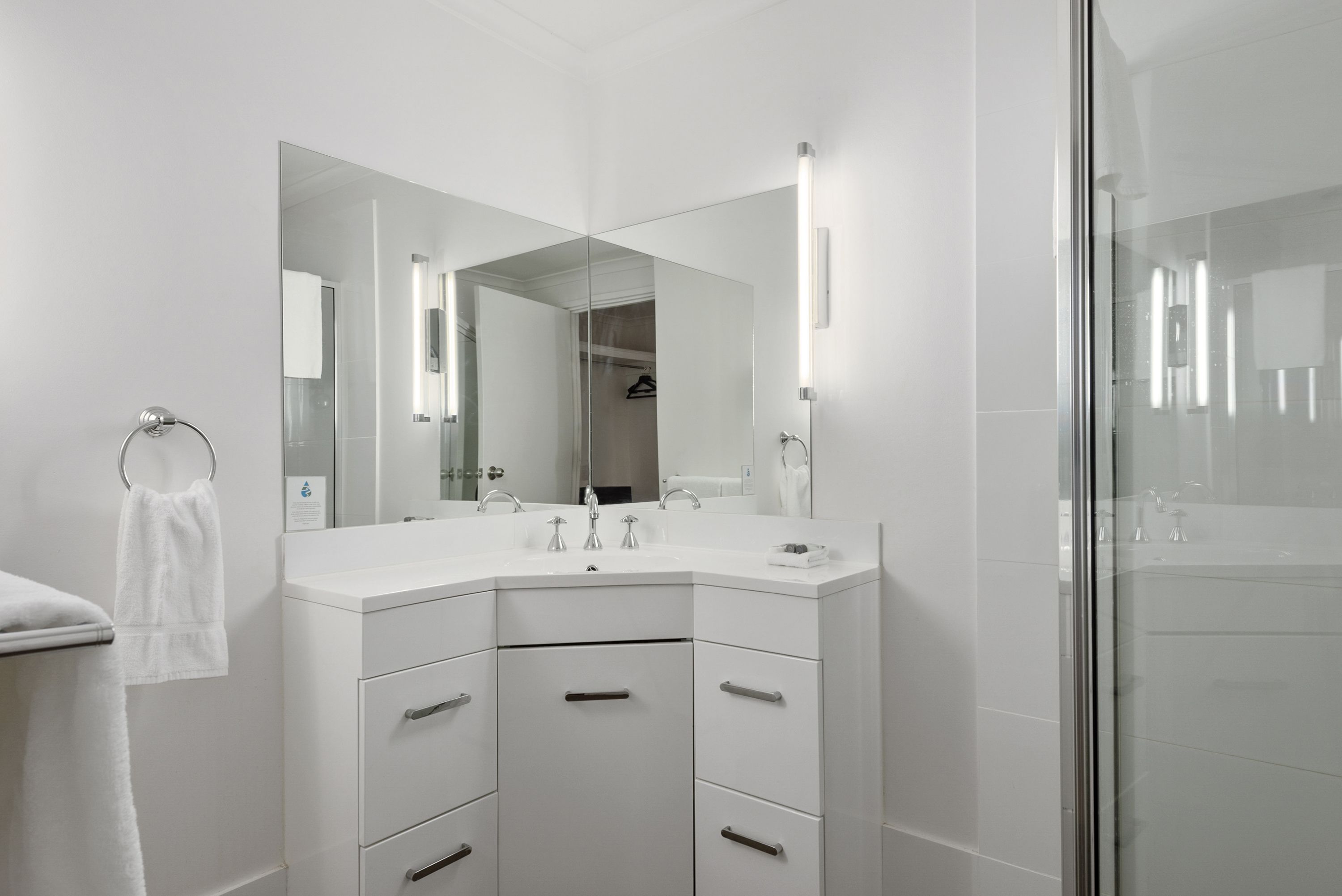 A modern bathroom with a white vanity, a large mirror, and a glass shower enclosure.