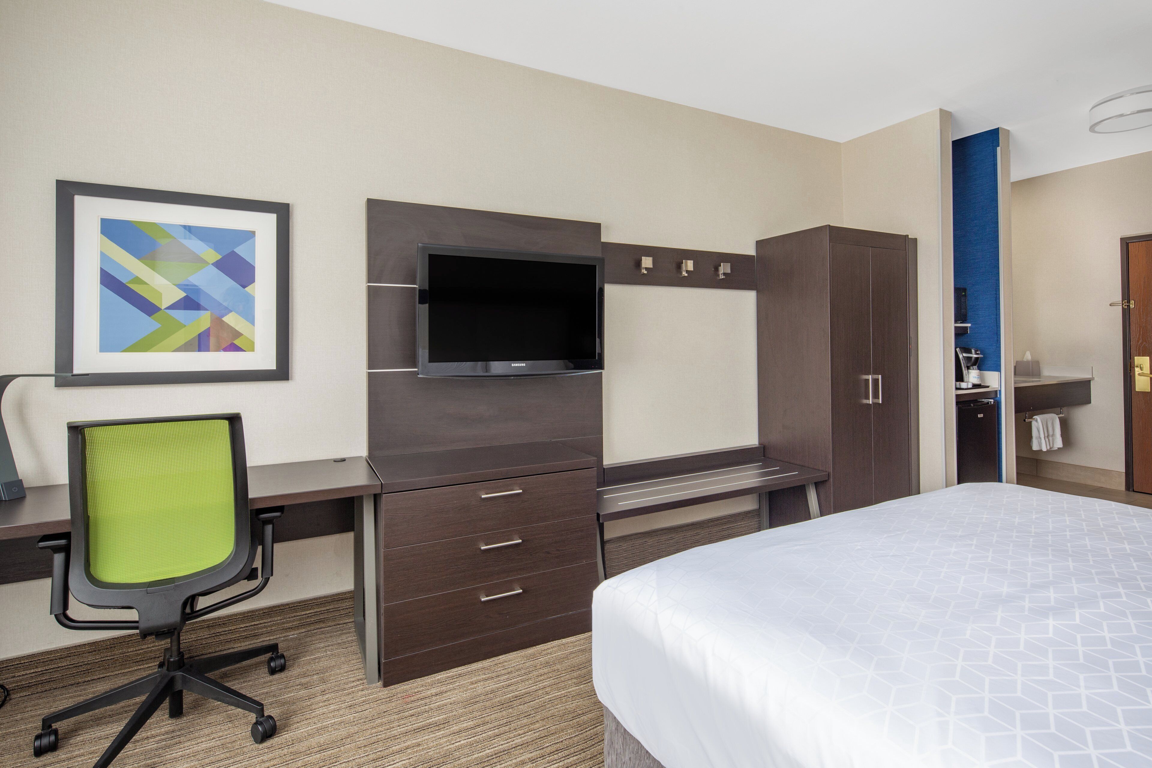 Una habitación de hotel con una cama, un escritorio con una silla, un televisor y un armario.