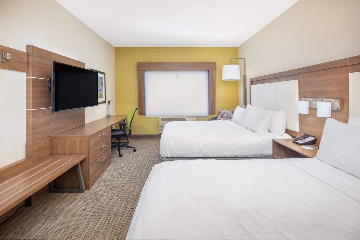 A hotel room with two beds, a desk, a chair, a TV, and a window.