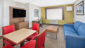 A compact hotel room with a dining area, a sofa, a TV mounted on the wall, and a window with blinds. - Holiday Inn Express Hotel & Suites Bishop by IHG (Bishop)