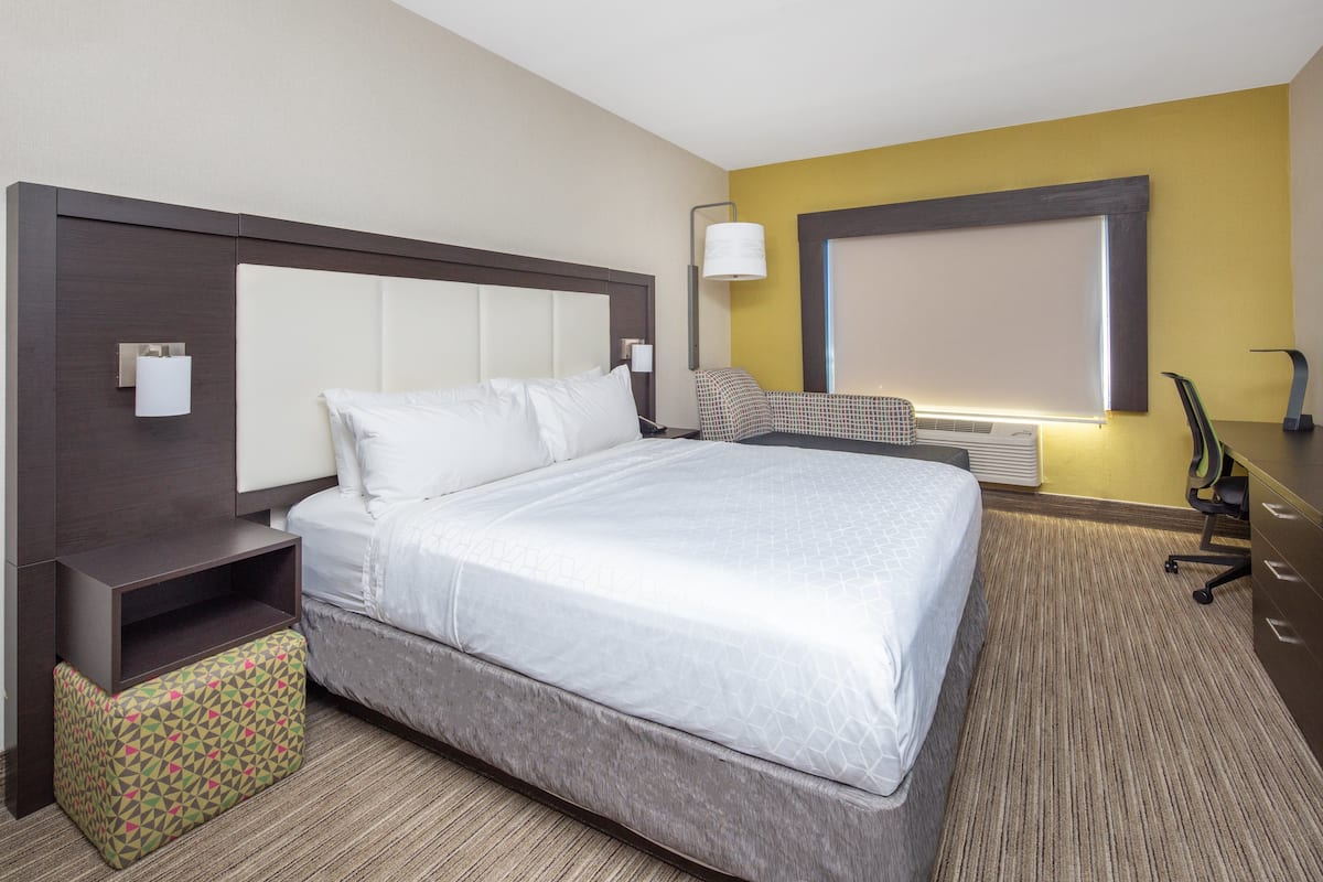A hotel room with a large bed, a desk, a chair, and a small table.