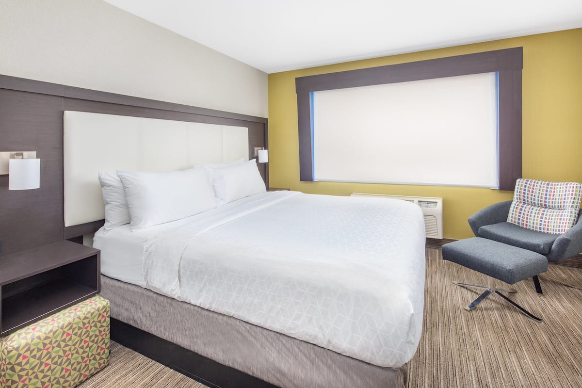 A hotel room with a large bed, a chair, a small table, and a window.