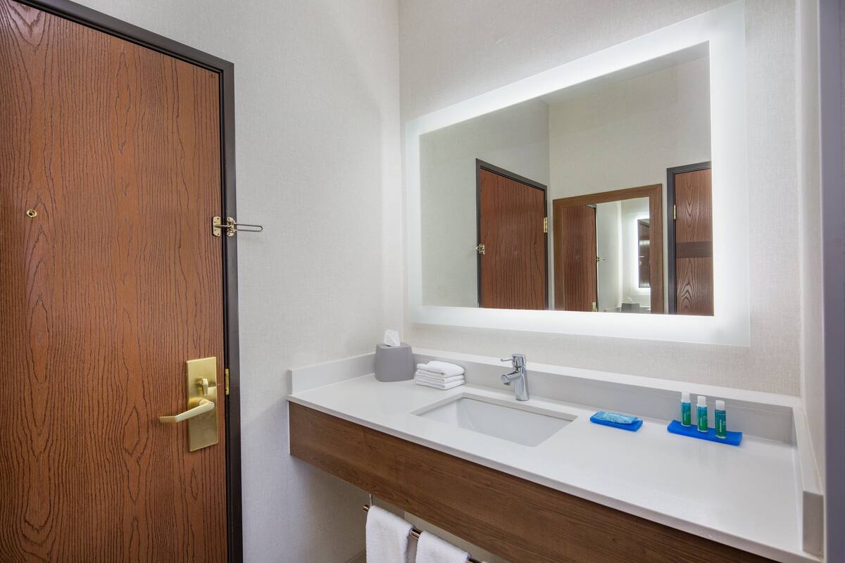 A bathroom with a wooden door, a white sink, a mirror, and toiletries on the counter.