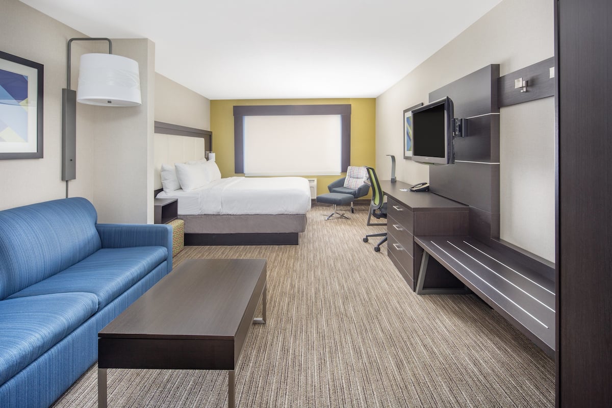 A hotel room with a bed, a blue sofa, a desk, a television, and a large window.