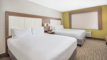 Quarto de hotel com duas camas, cabeceira de madeira, mesa de cabeceira com telefone e janela com persianas.