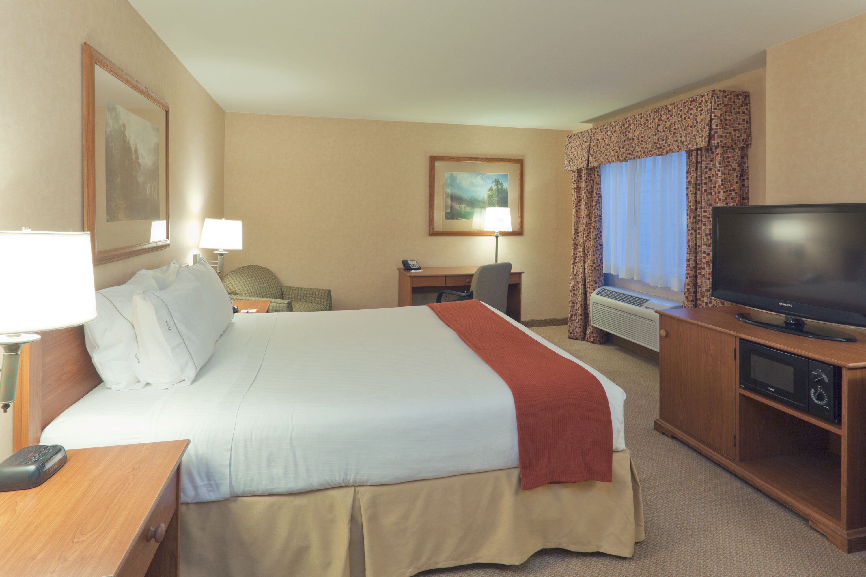 A hotel room with a bed, a desk, a chair, a television, and a window with curtains.