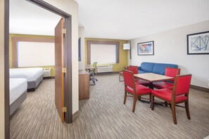 Une chambre d’hôtel avec deux lits, un bureau, une table avec des chaises rouges et un canapé bleu.