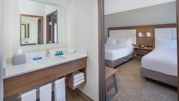 A hotel room with a large mirror, a sink, a vanity, two beds, and a nightstand with lamps. - Holiday Inn Express Hotel & Suites Bishop by IHG (Bishop)