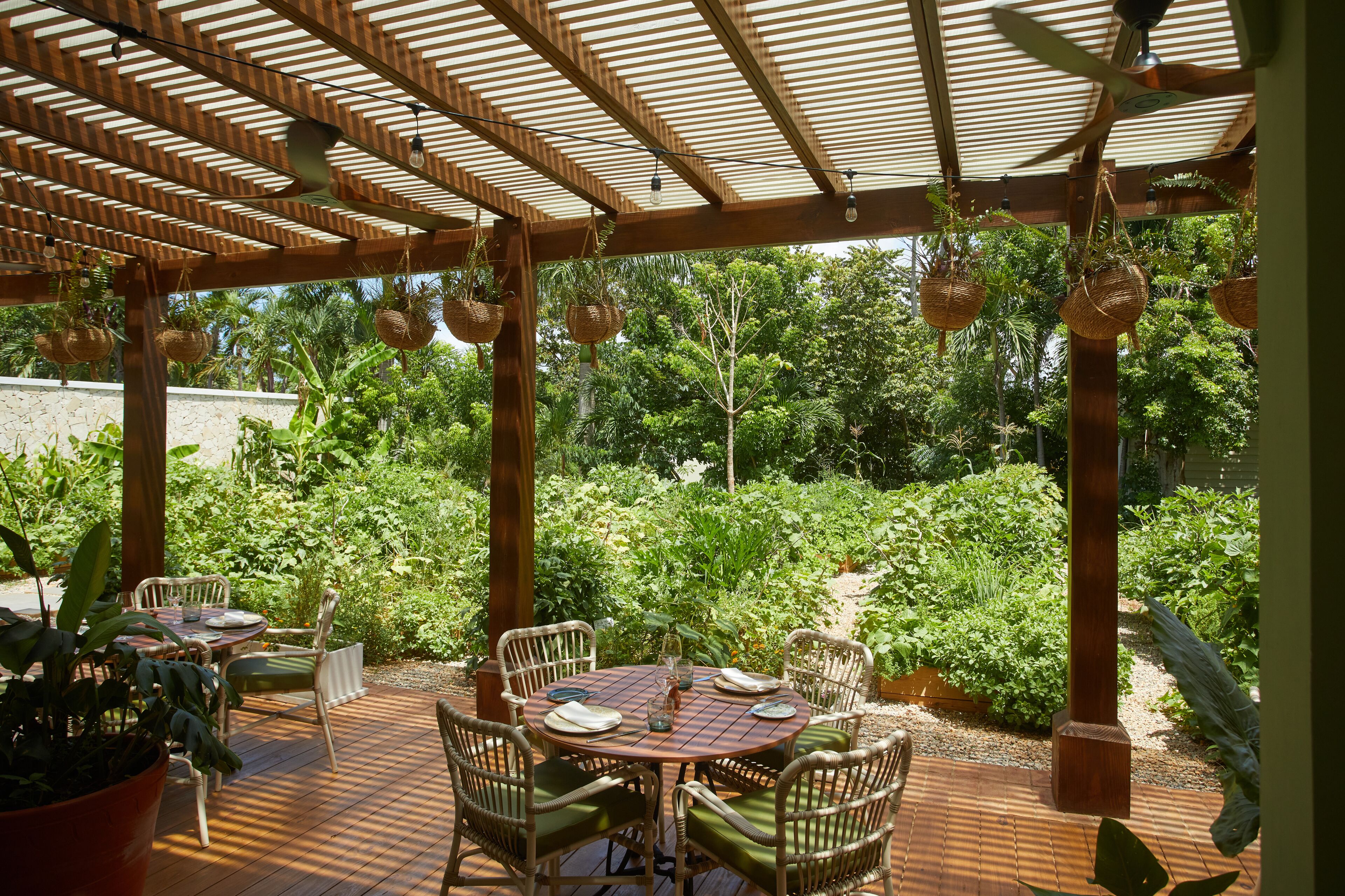 An outdoor patio with a wooden pergola, wicker chairs, and a table set for dining.