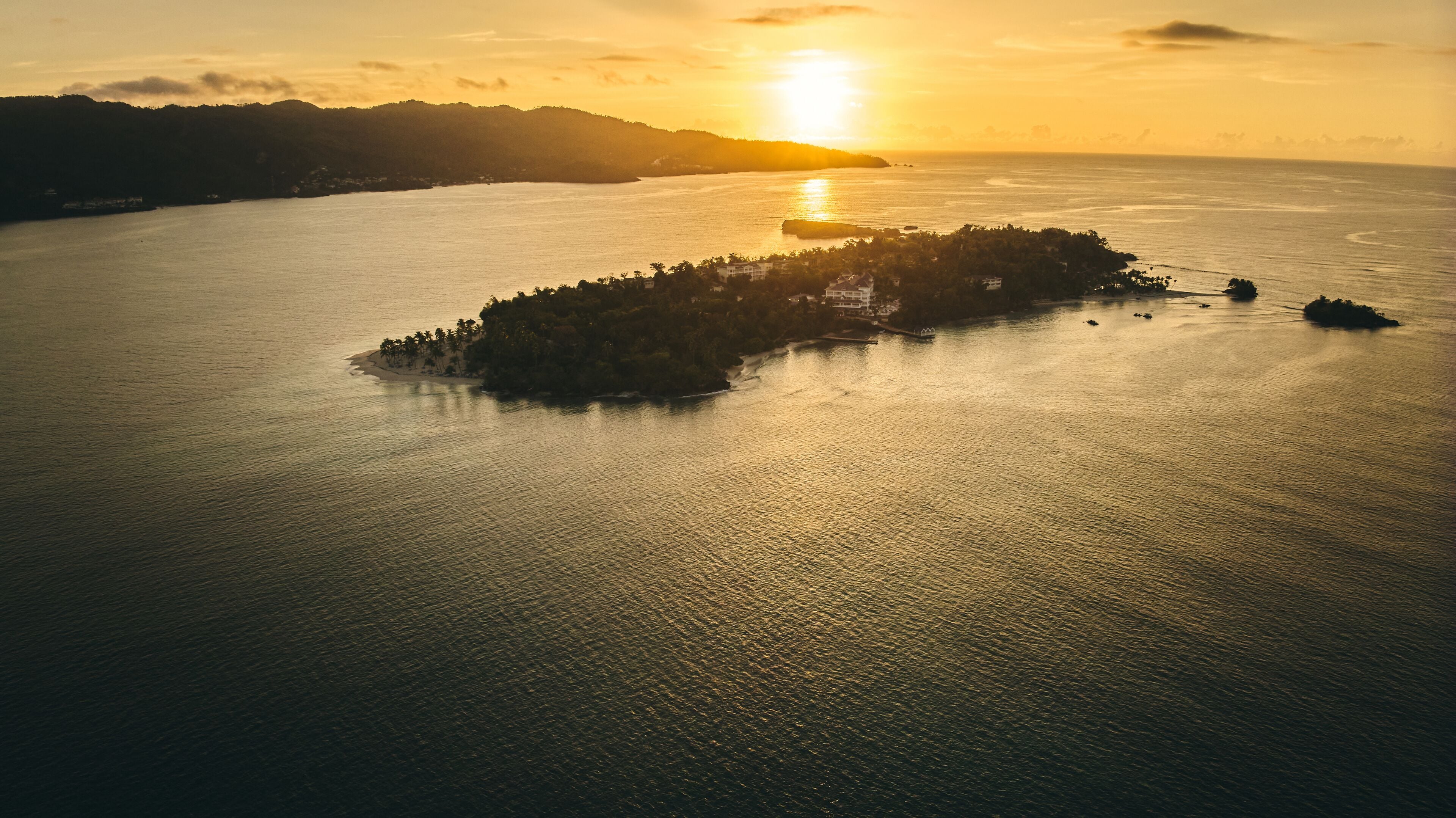 An aerial view of a coastal area with a small island surrounded by water, featuring a sunset in the background.