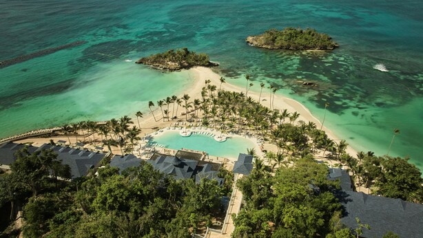 Vista aerea di un resort con piscina centrale, diverse zone sulla spiaggia e vegetazione lussureggiante.